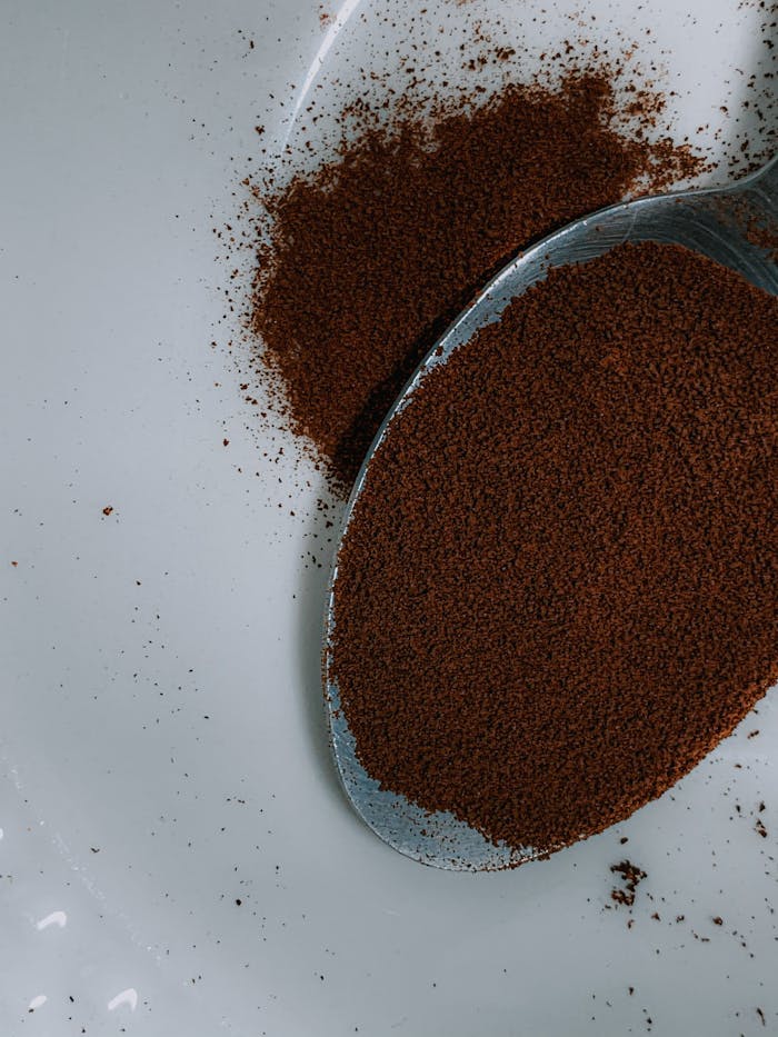 Close-up of ground coffee on a spoon, showcasing rich aroma and texture.